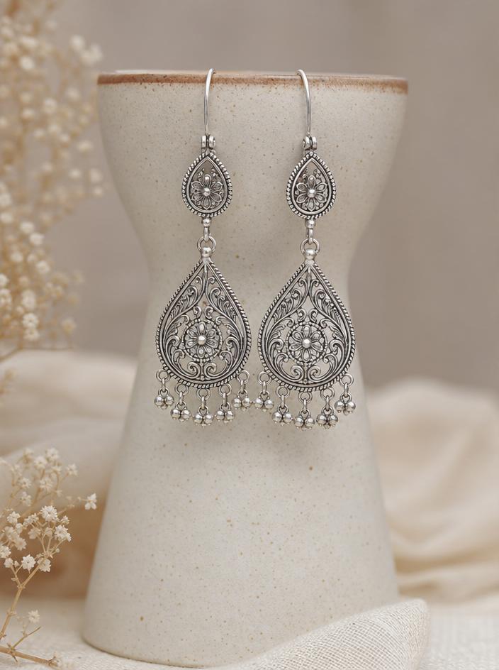 Delicate silver drop earrings hanging from a ceramic stand